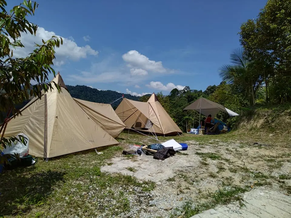 Outdoor camping tents set up on a hill in Malaysia surrounded by tropical trees and blue sky, ideal for team-building retreats and nature-based activities.