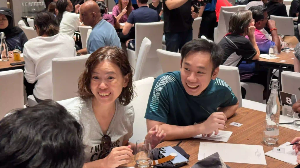 Two participants from Vision Building are smiling and actively engaged in a discussion at a table during a team-building event, reflecting a moment of shared awareness and connection that leads to positive change.