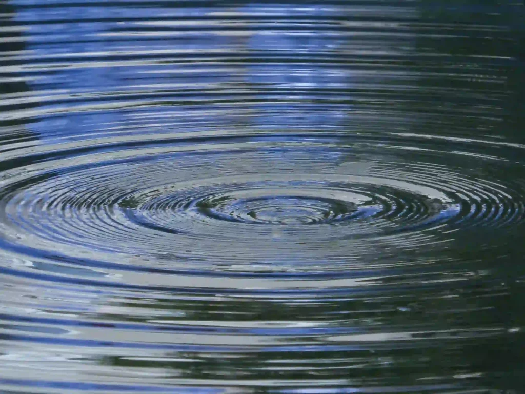 Close-up shot of concentric ripples spreading outward on a calm, reflective water surface, visually representing the ripple effect of a clear purpose.
