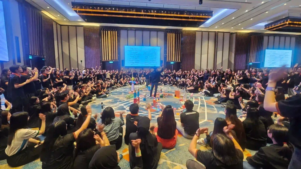 A small group of professionals from Vision Building are seated on the carpet in a circle, engaged in a hands-on team-building activity. They are surrounded by colorful materials and appear to be discussing or collaborating on a task, demonstrating focused engagement and intentional practice during the Vision Building team event.