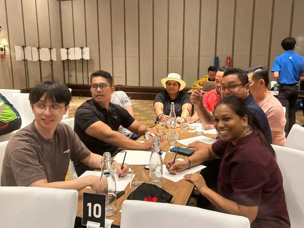 A group of costumer from Vision Building event are seated at a table, smiling and taking notes. The image captures the collaborative process of translating team-building activities into practical and actionable applications.