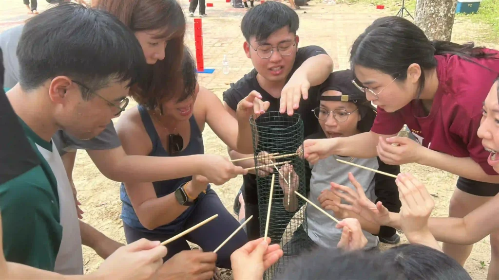 Diverse team members intently collaborating on a difficult dexterity challenge with sticks.