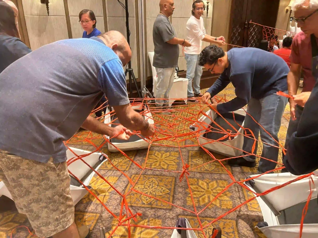 Vision Building participants collaboratively manage a complex red rope network indoors, demonstrating problem-solving in an integrated corporate training session.