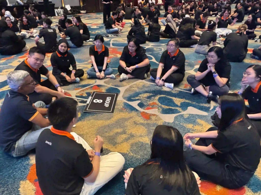 Team members, including leadership, sitting in a circle on the floor, deeply engaged in discussion during an indoor workshop, symbolizing listening and psychological safety.
