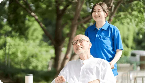 介護職員と入居者が屋外で一緒に過ごす様子。施設の庭での交流風景。
