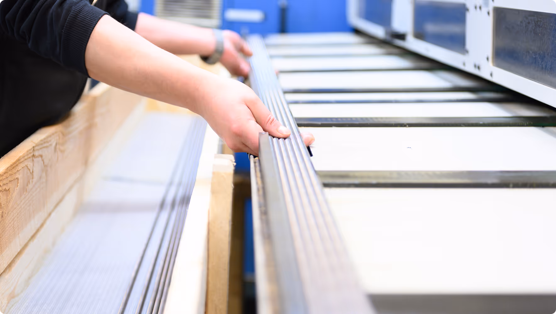 Person hält lange, metallische, geriffelte Schiene an einer Industriemaschine.