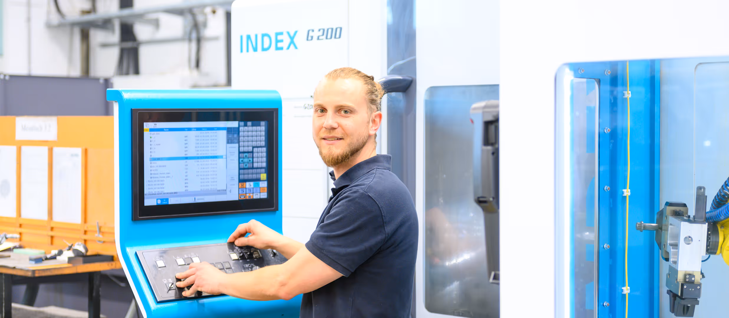 Techniker bedient CNC-Maschine INDEX G 200 mit Touchscreen und Bedienelementen in einer Werkstatt.