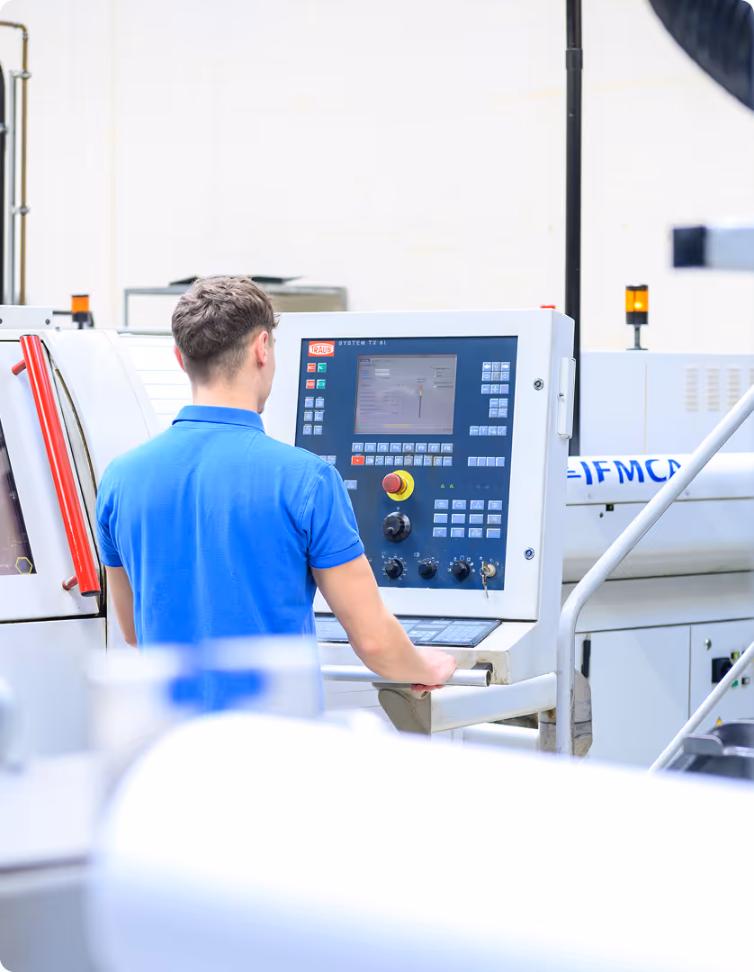 Mann in blauem Hemd bedient eine CNC-Maschine mit Steuerpult im Industrieumfeld.