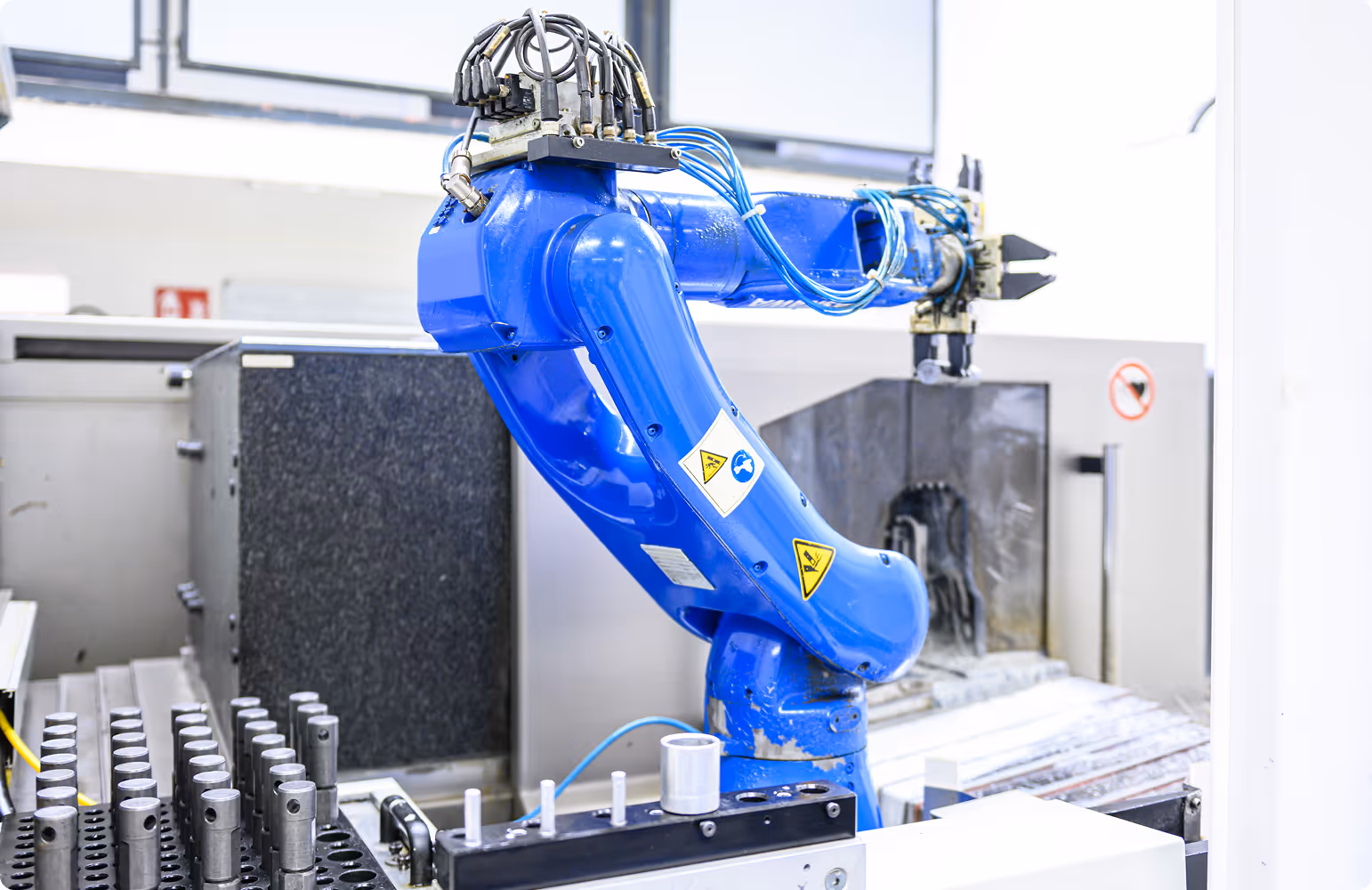 Blauer Industrieroboterarm in einer Fertigungsanlage mit Metallteilen in der Nähe.