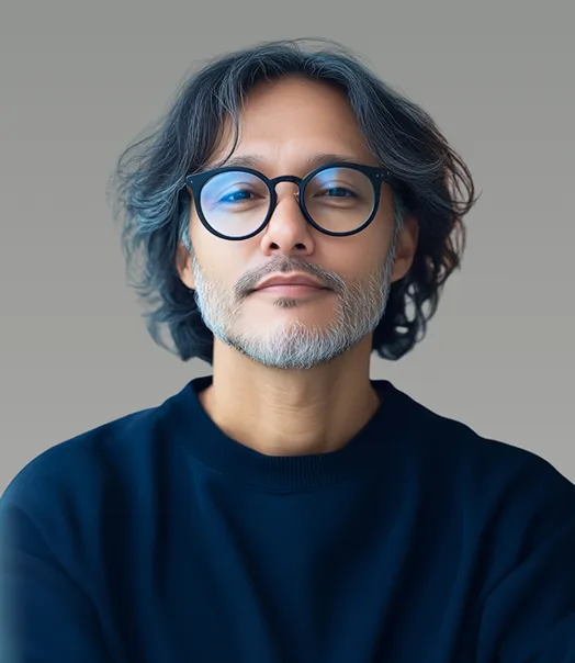 Portrait of a middle-aged man with medium-length wavy gray hair, beard, and round glasses wearing a dark blue sweater.
