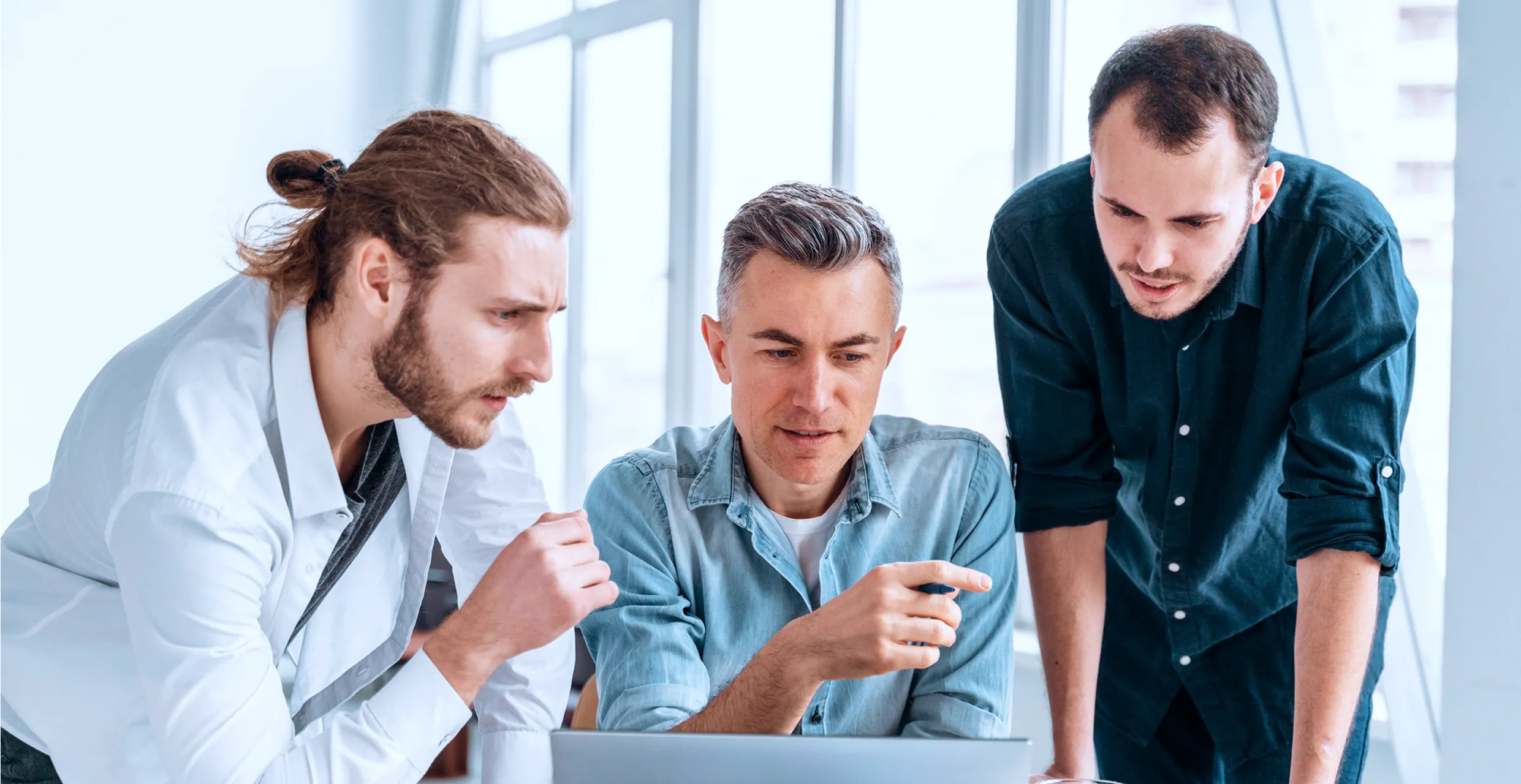 Three men focused on a laptop screen in a bright office setting.