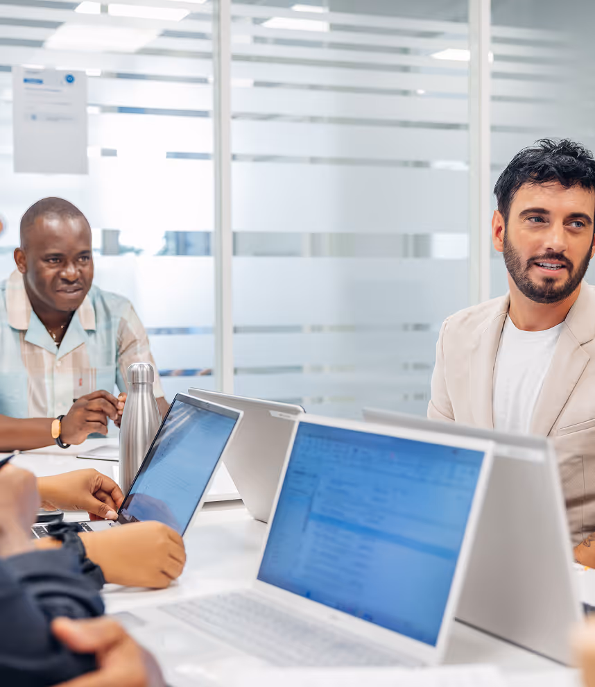 Un groupe de professionnels discutant lors d'une réunion de travail avec des ordinateurs portables sur la table dans un bureau moderne.