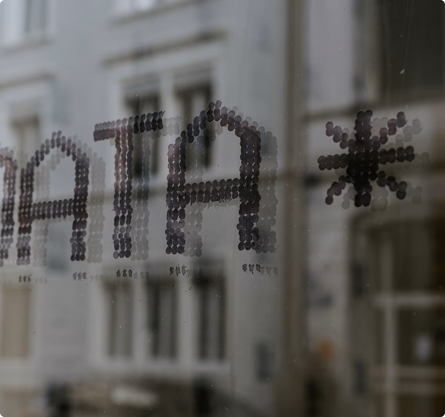 Reflet flou de bâtiments urbains vus à travers une vitre avec un motif en points formant le mot partiel 'DATA' et un astérisque.