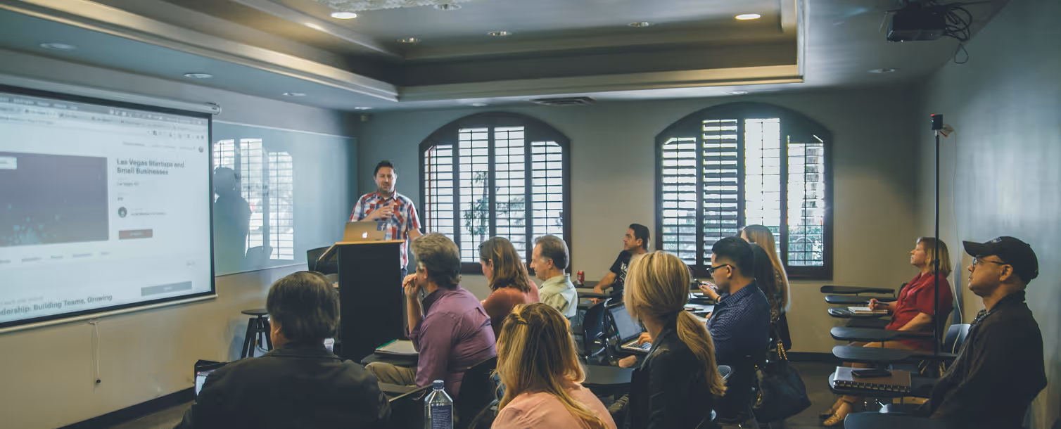 Un homme donne une présentation avec un ordinateur portable devant un groupe de personnes assises dans une salle de formation.