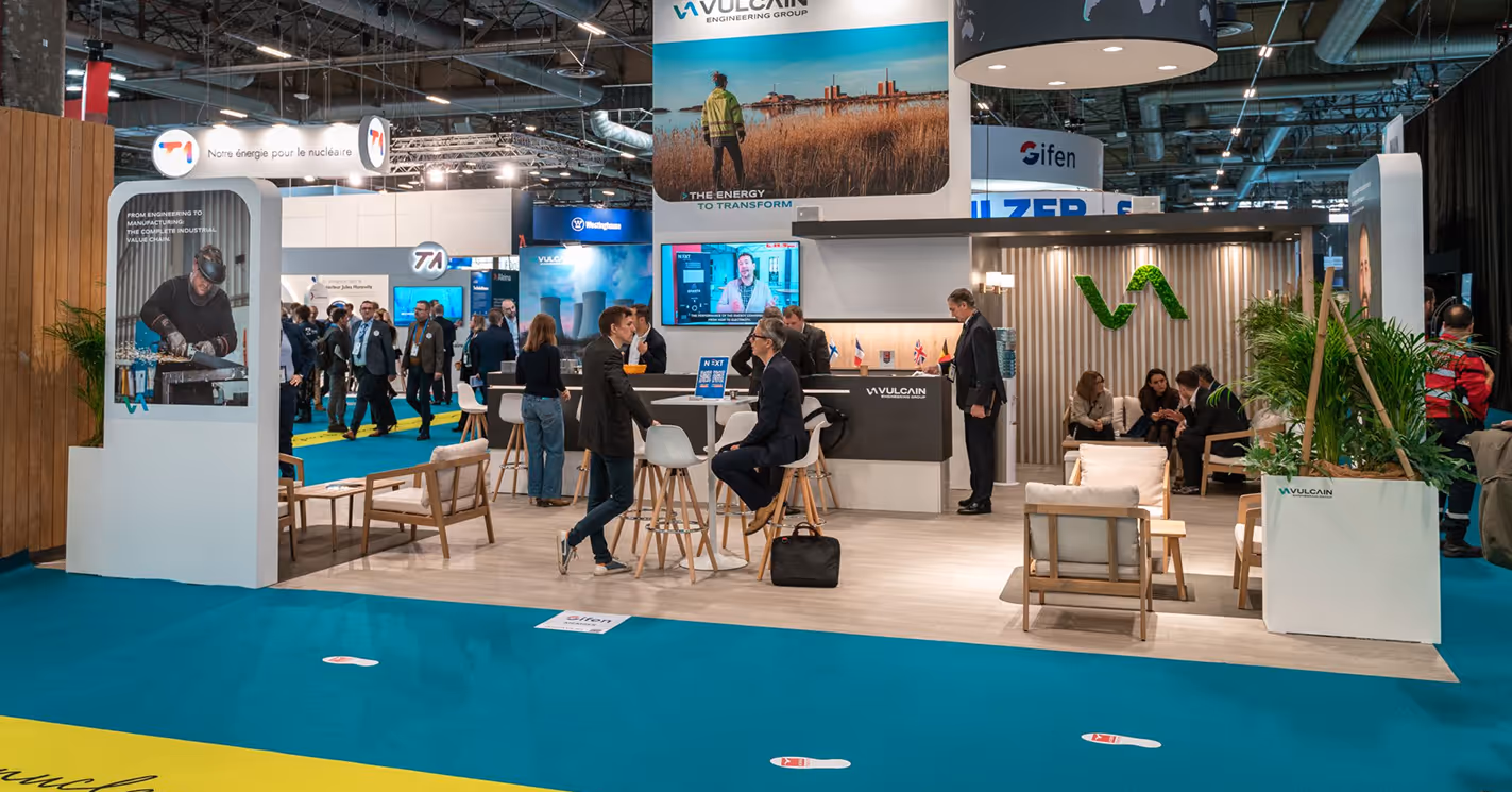 Stand exposant moderne Vulcain Engineering Group avec des personnes discutant et assises dans un espace lumineux et aéré lors d'un salon professionnel.