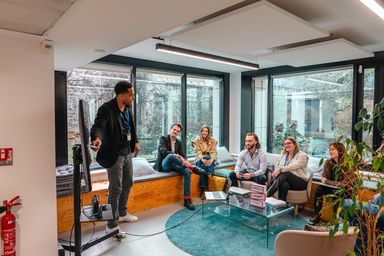 Un homme donne une présentation à un groupe assis dans un bureau lumineux avec de grandes fenêtres.