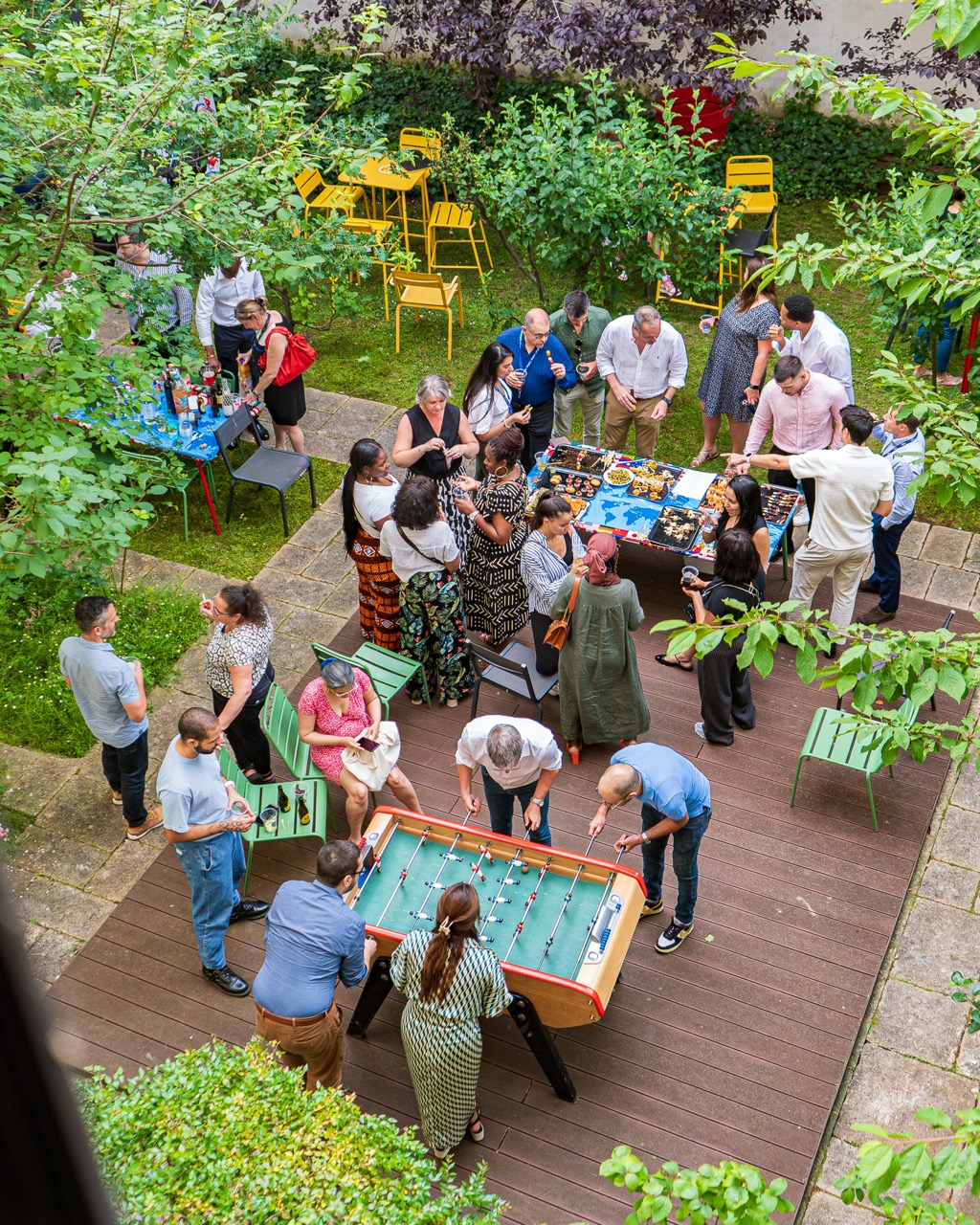 Groupe de personnes jouant au baby-foot et discutant lors d'une fête en plein air dans un jardin.
