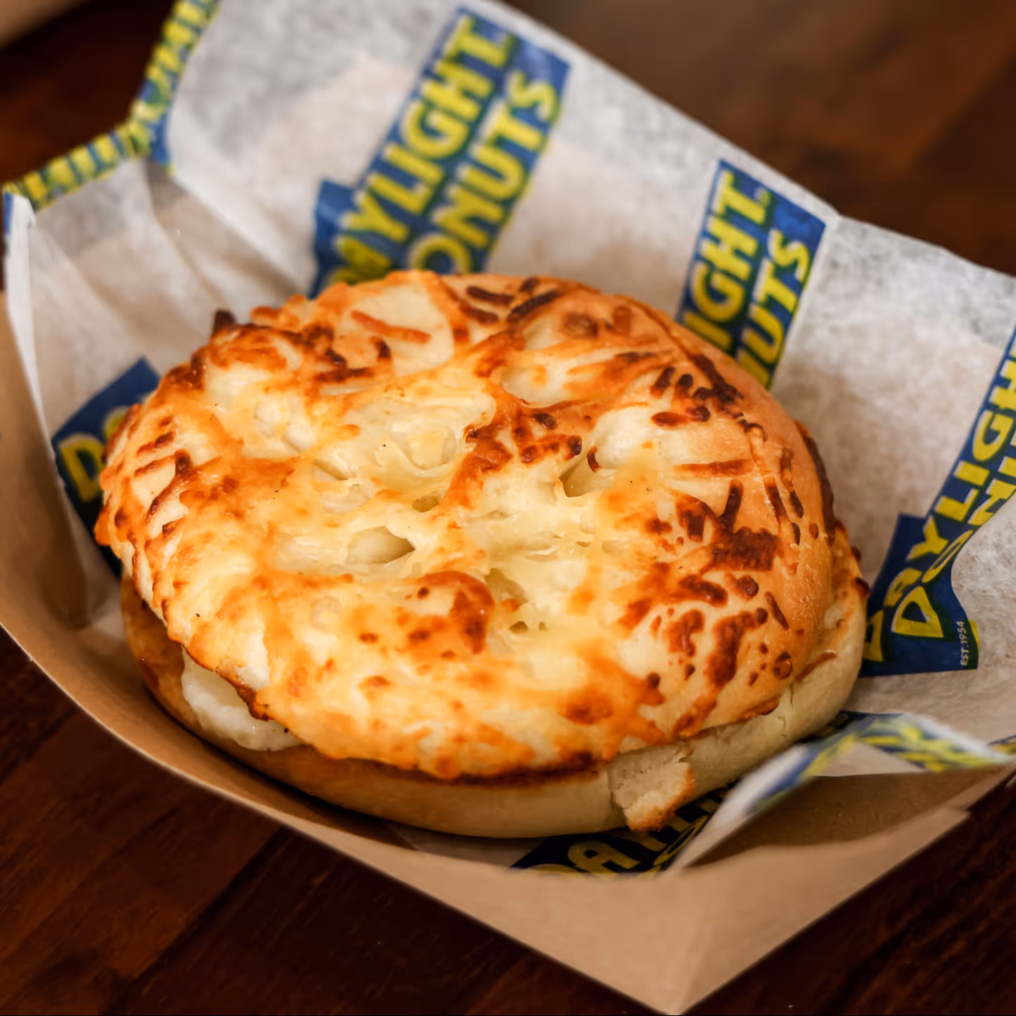 Close-up of a toasted cheese bagel sandwich served in a paper-lined tray with daylight donuts branding.