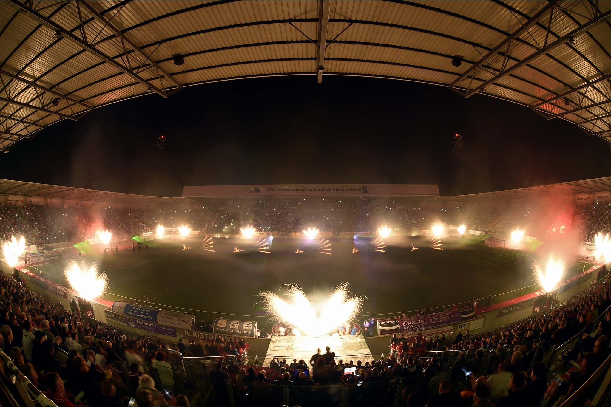 Spectacle pyrotechnique explosant au dessus des tribunes d'un stade bondé sous toit incurvé