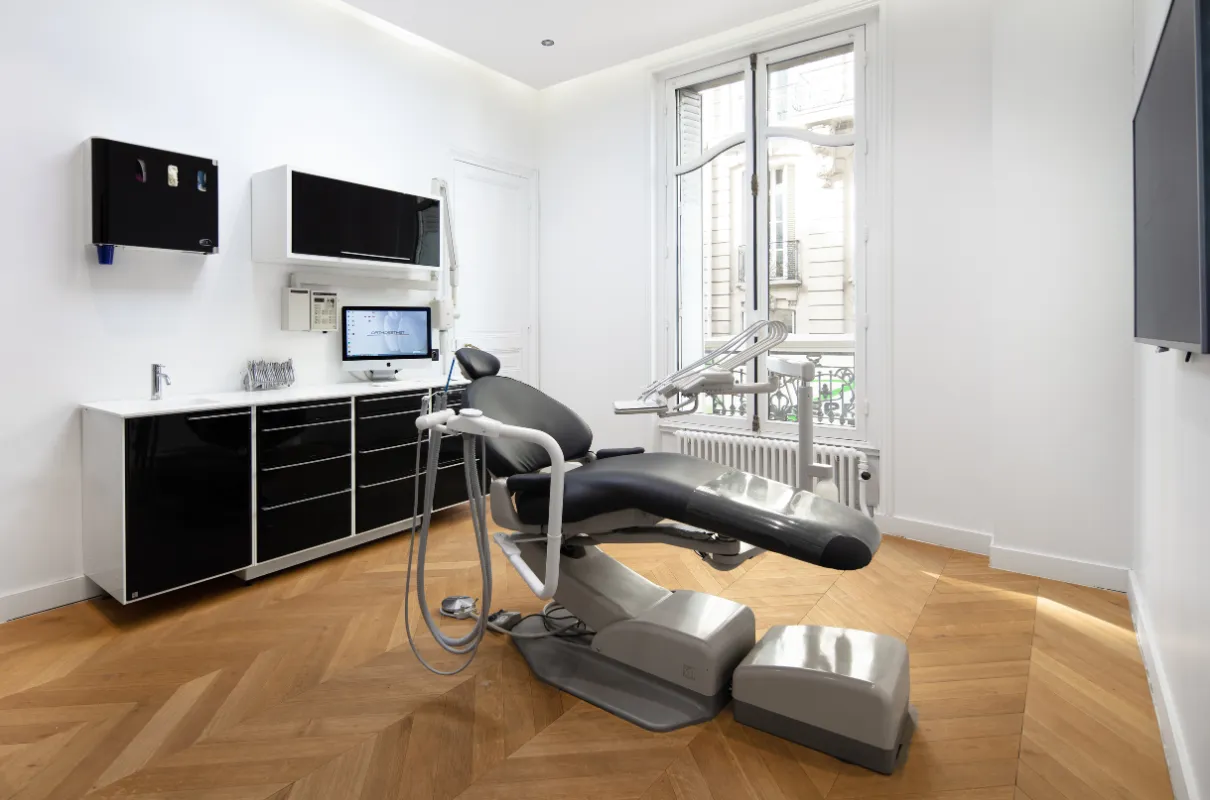 Salle de consultation dentaire moderne avec fauteuil noir, grande fenêtre et comptoir noir brillant.