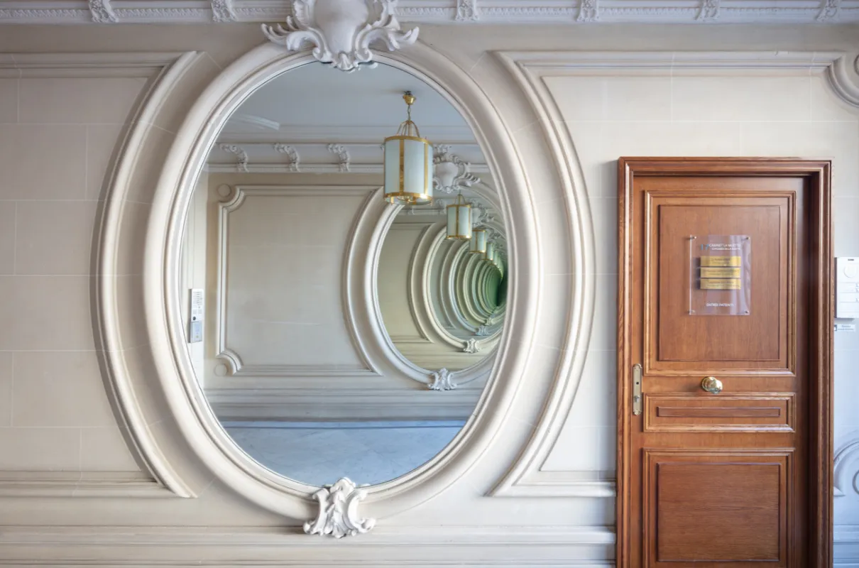 Miroir mural ovale sculpté reflétant un effet infini à côté d'une porte en bois ornée.