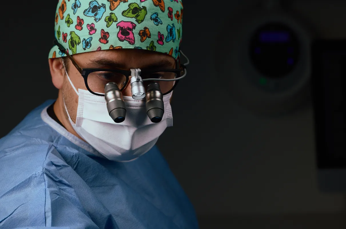 Chirurgien portant une coiffe colorée, un masque et des loupes dentaire pour soins précis.