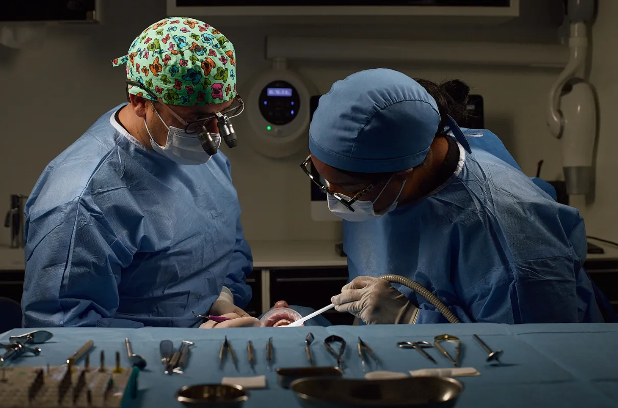 Deux chirurgiens dentistes en tenue opératoire effectuent une intervention dentaire en salle sterile.