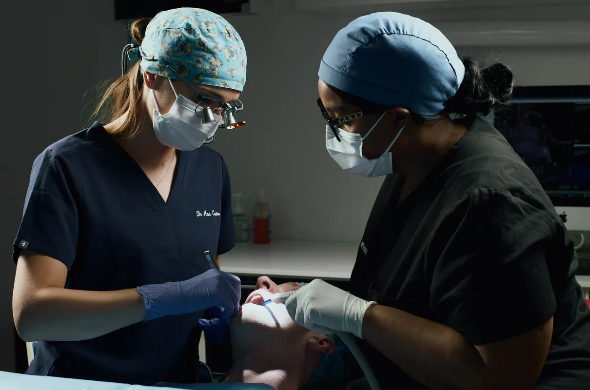 Deux chirurgiens dentistes portant des masques et des gants soignent un patient allongé en cabinet dentaire.