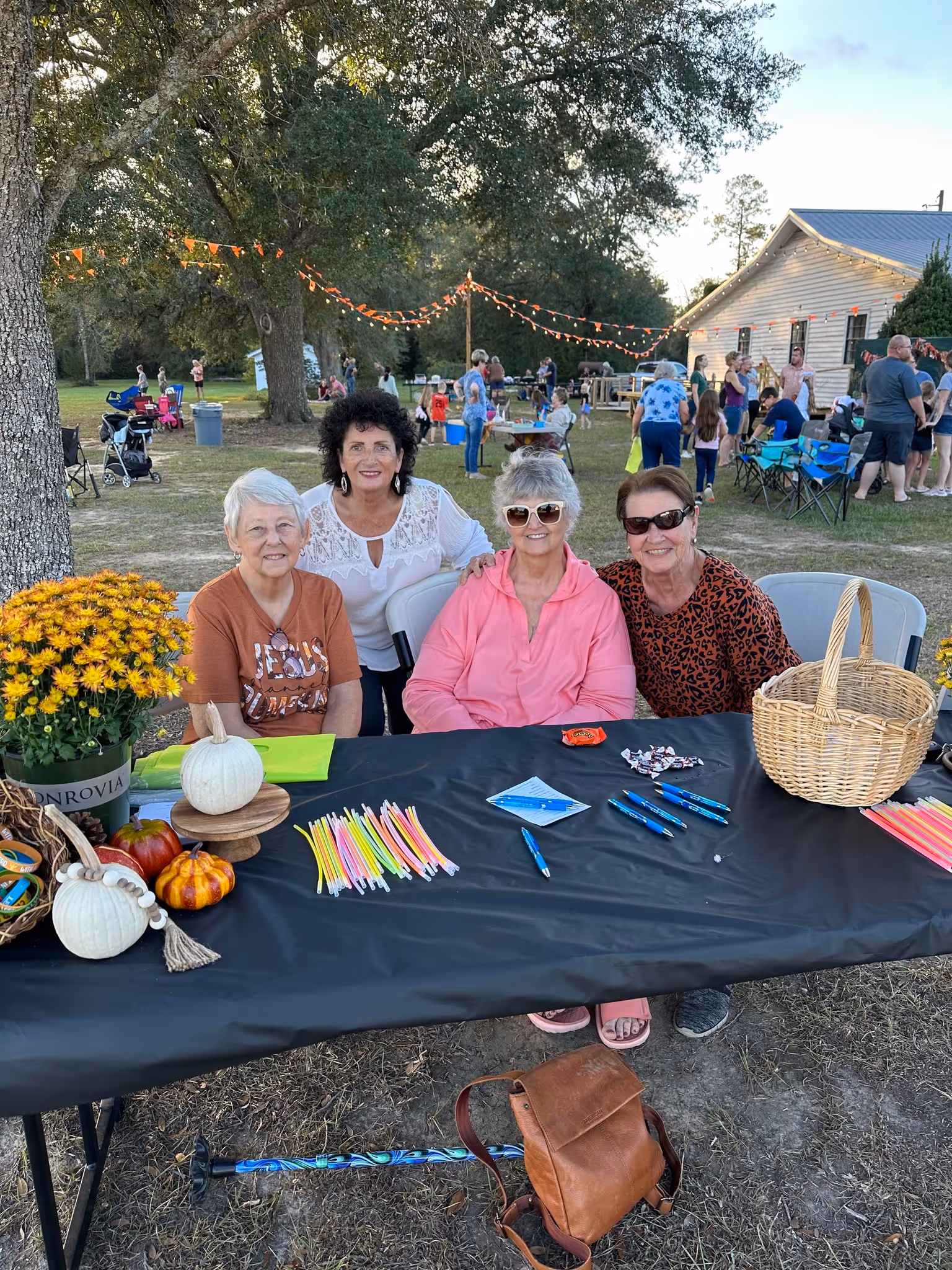Four senior women smiling at a table with fall decorations at an outdoor community event.
