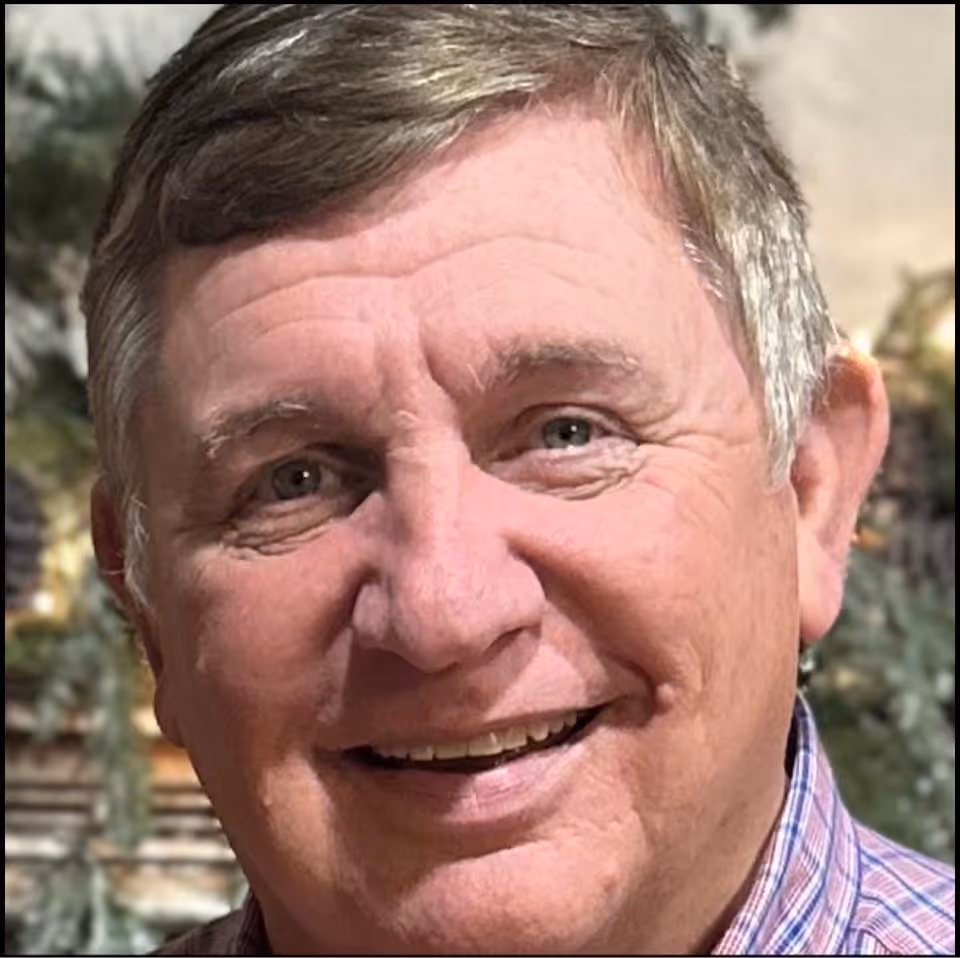 Close-up of a smiling older man with gray hair wearing a checkered shirt.