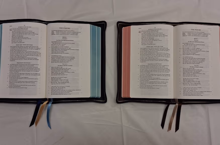 Two open Bibles showing the Book of Psalms with different colored ribbons on a white cloth.