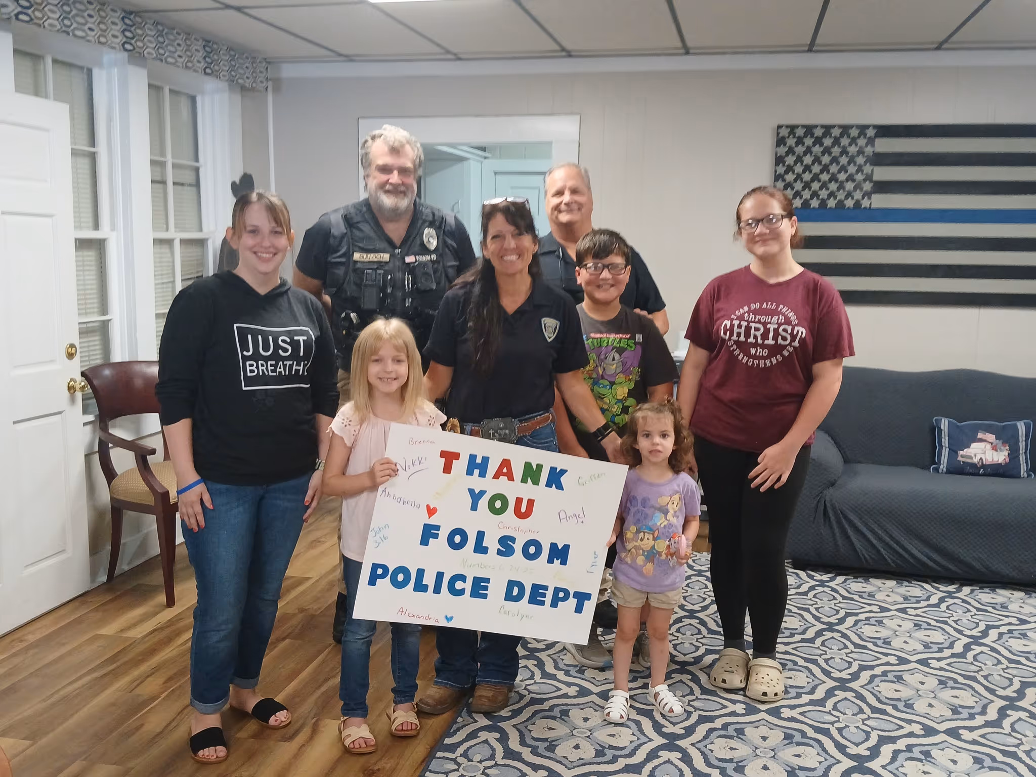 Group of children and police officers holding a sign saying 'Thank You Folsom Police Dept' inside a room.