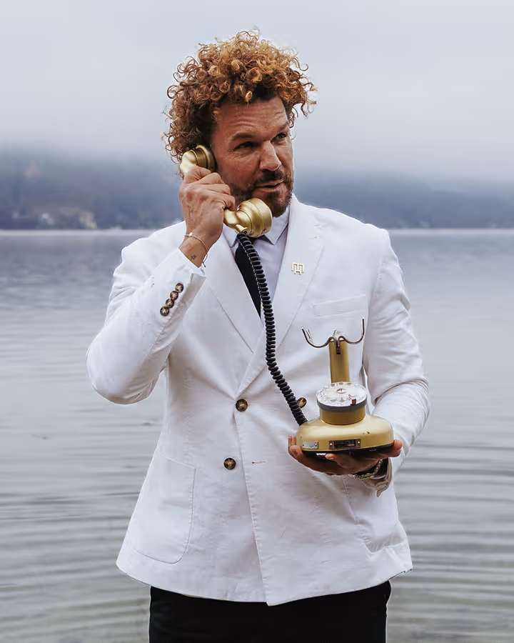 Mario Hofferer wearing a white suit with an old golden phone in his hand.