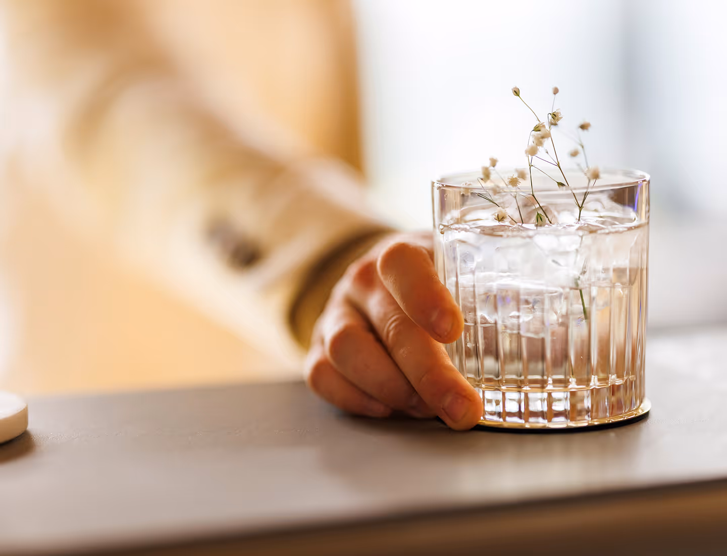 Hand holding a glass with ice cubes and small white flowers on a table.