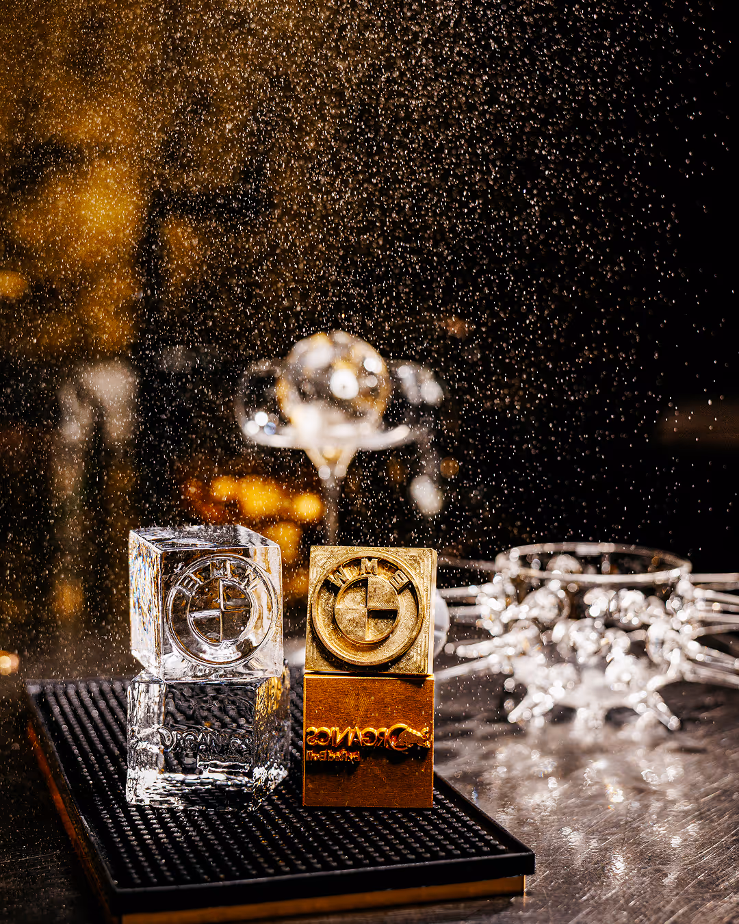 Two square awards, one gold and one silver, placed on a mat with sparkling droplets in the background.