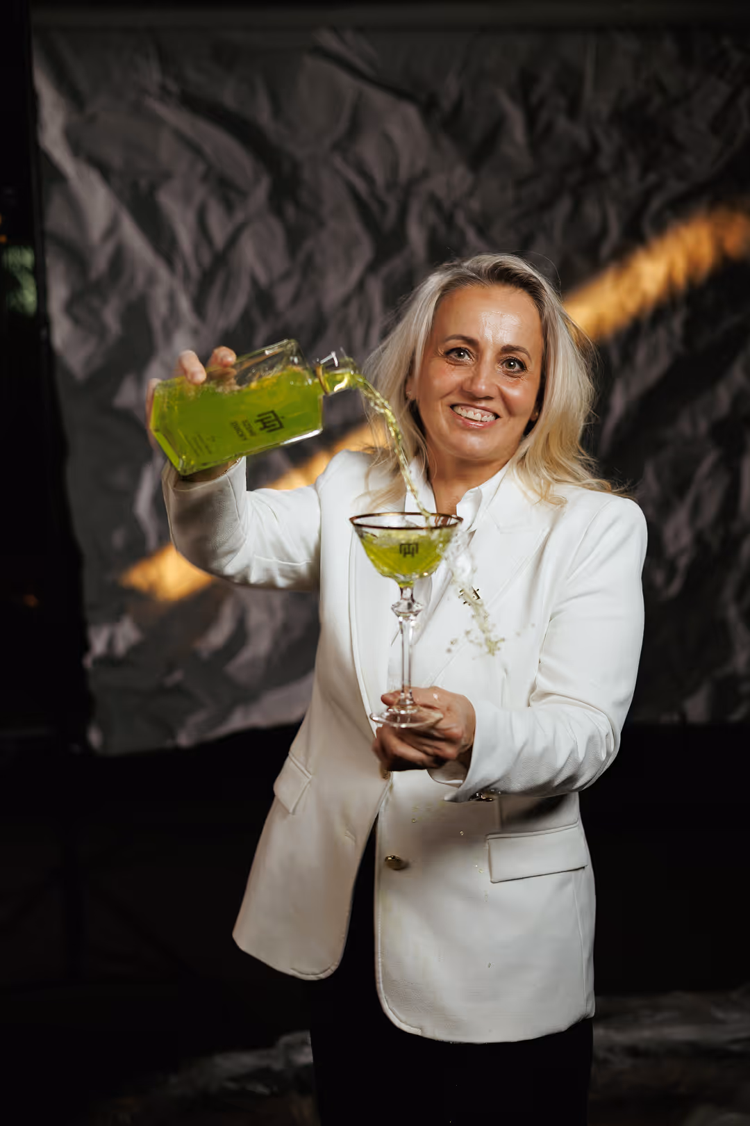 Portrait of Krisztina Borza in a white suit pouring a drink