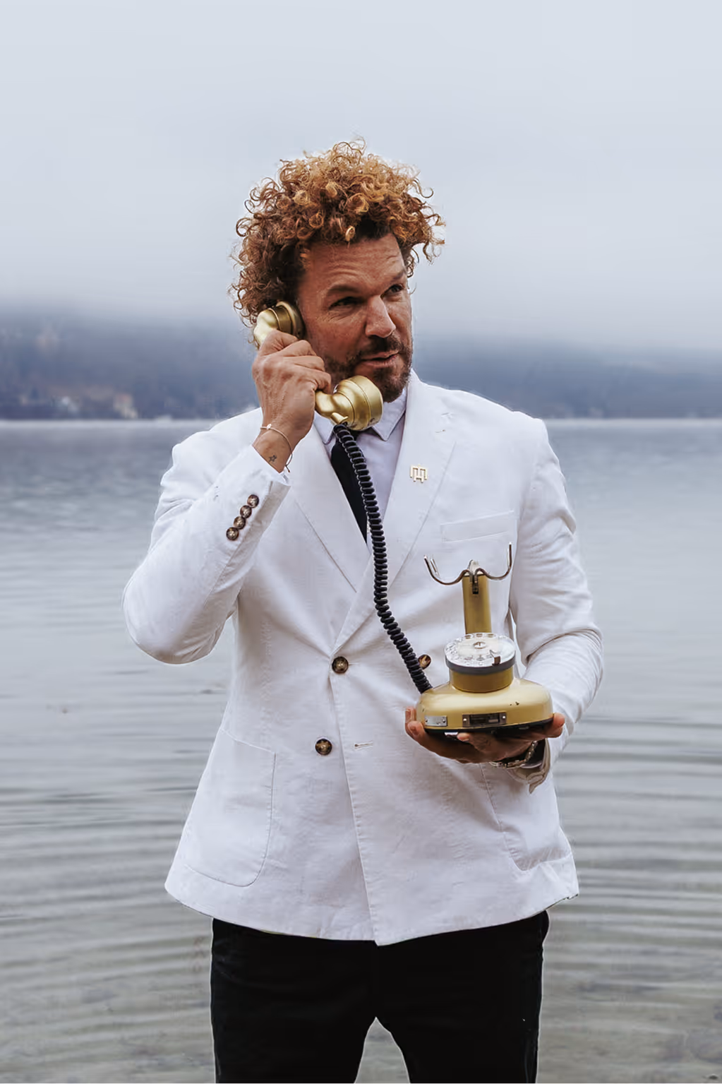 Mario Hofferer wearing a white suit with an old golden phone in his hand.