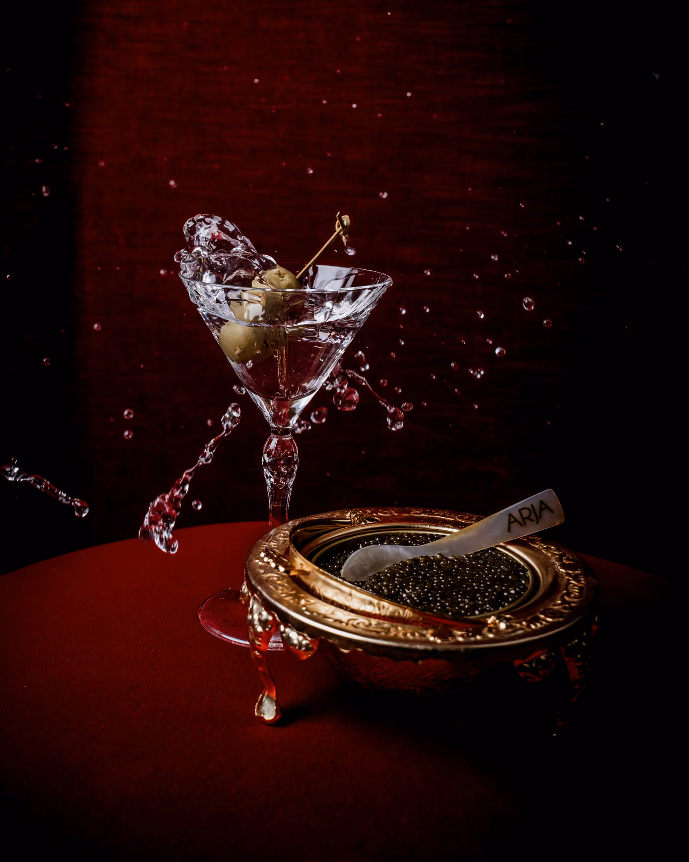 Man in a red suit holding a glass with liquid splashing out in an arc.