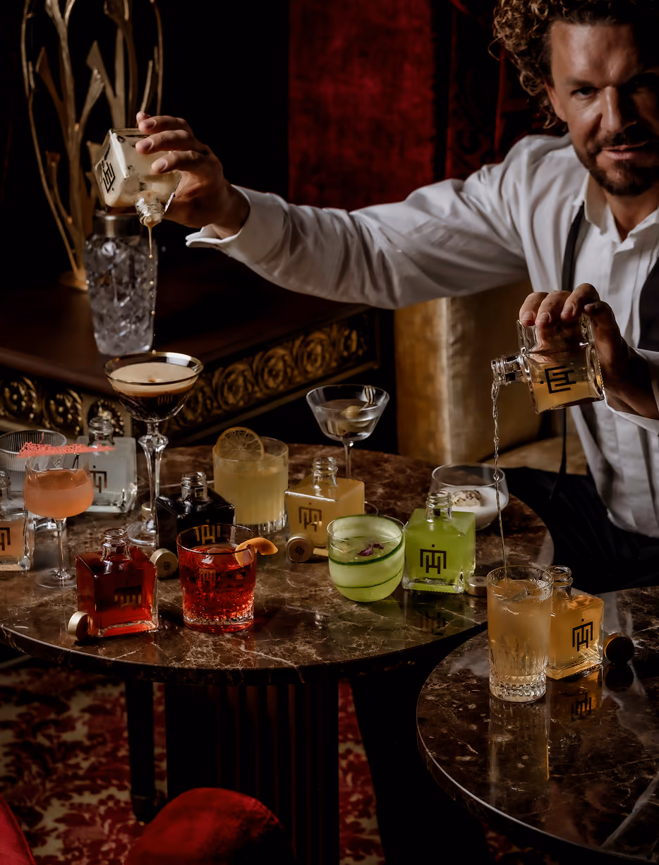 Mario Hofferer behind a table with various cocktails, pouring drinks from both hands.