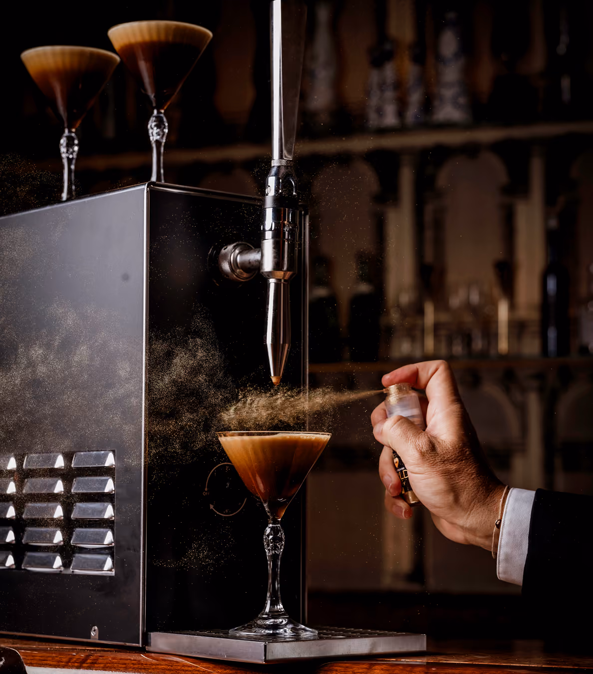 nitro machine with a cocktail in front, a hand sprays gold on it.