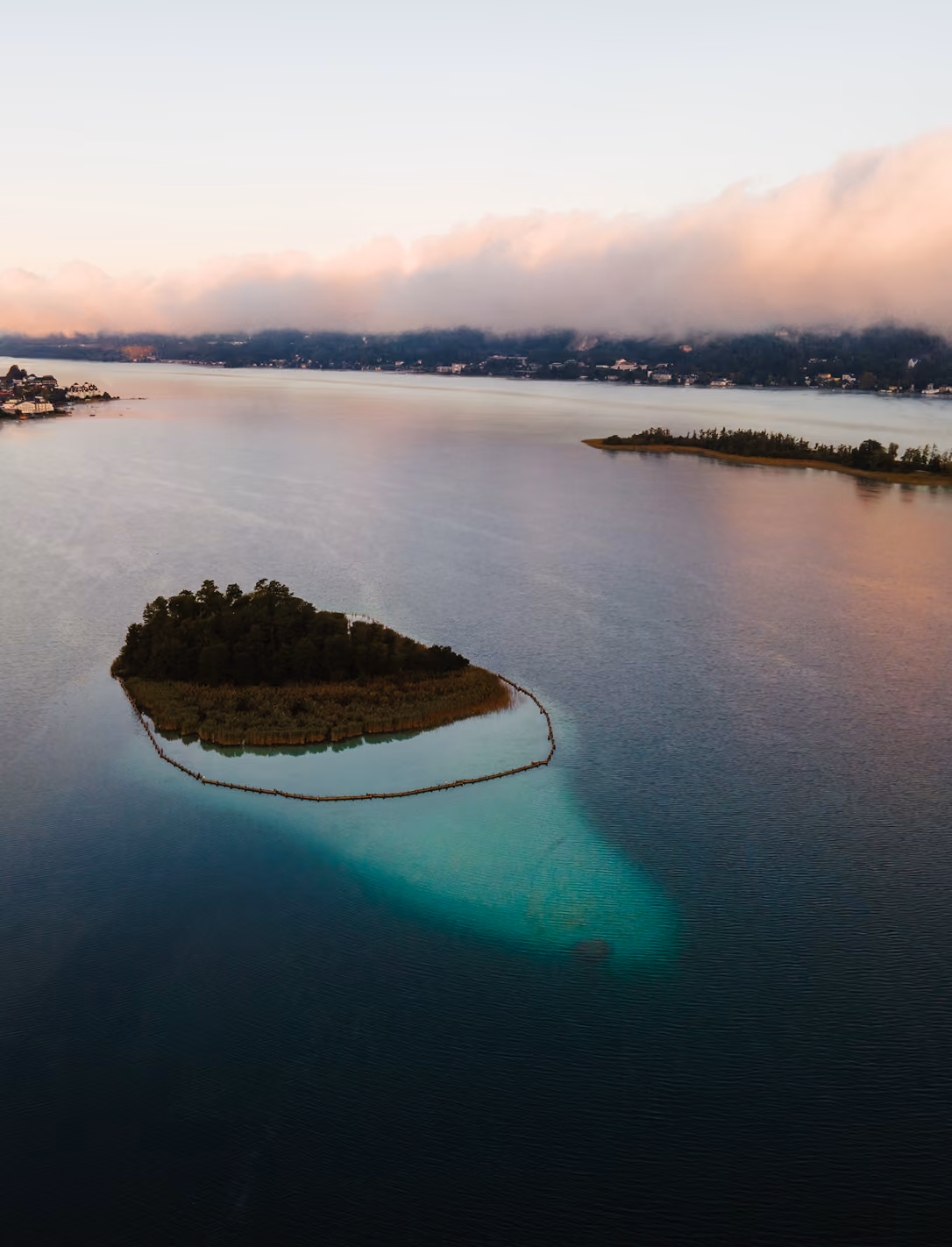 Aerial view of a small forested island in a calm lake with misty hills in the background.