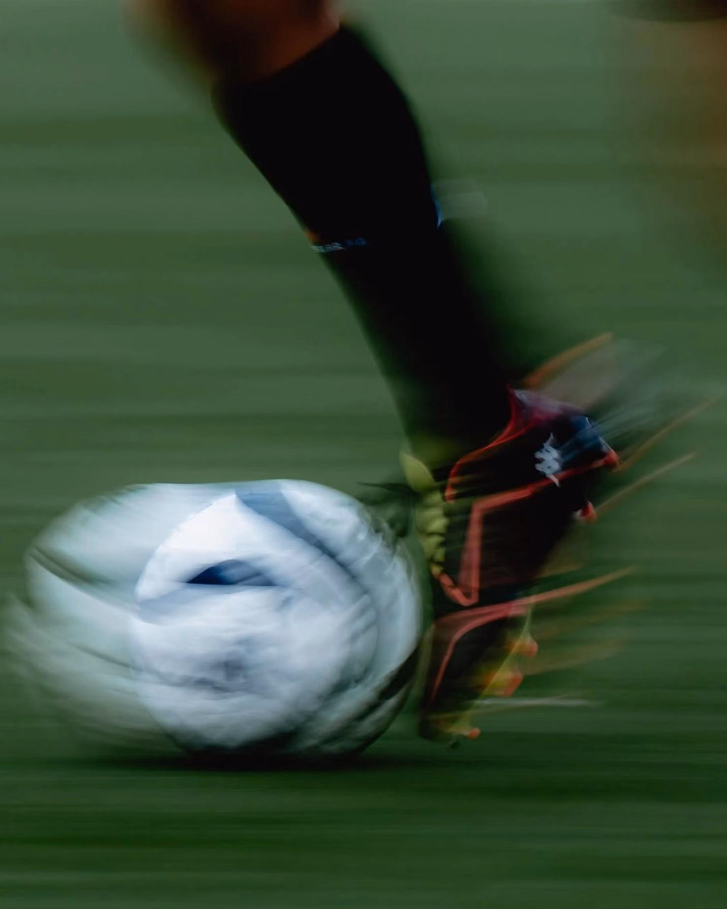 Blurred motion of a soccer player's foot kicking a white and black soccer ball on grass.