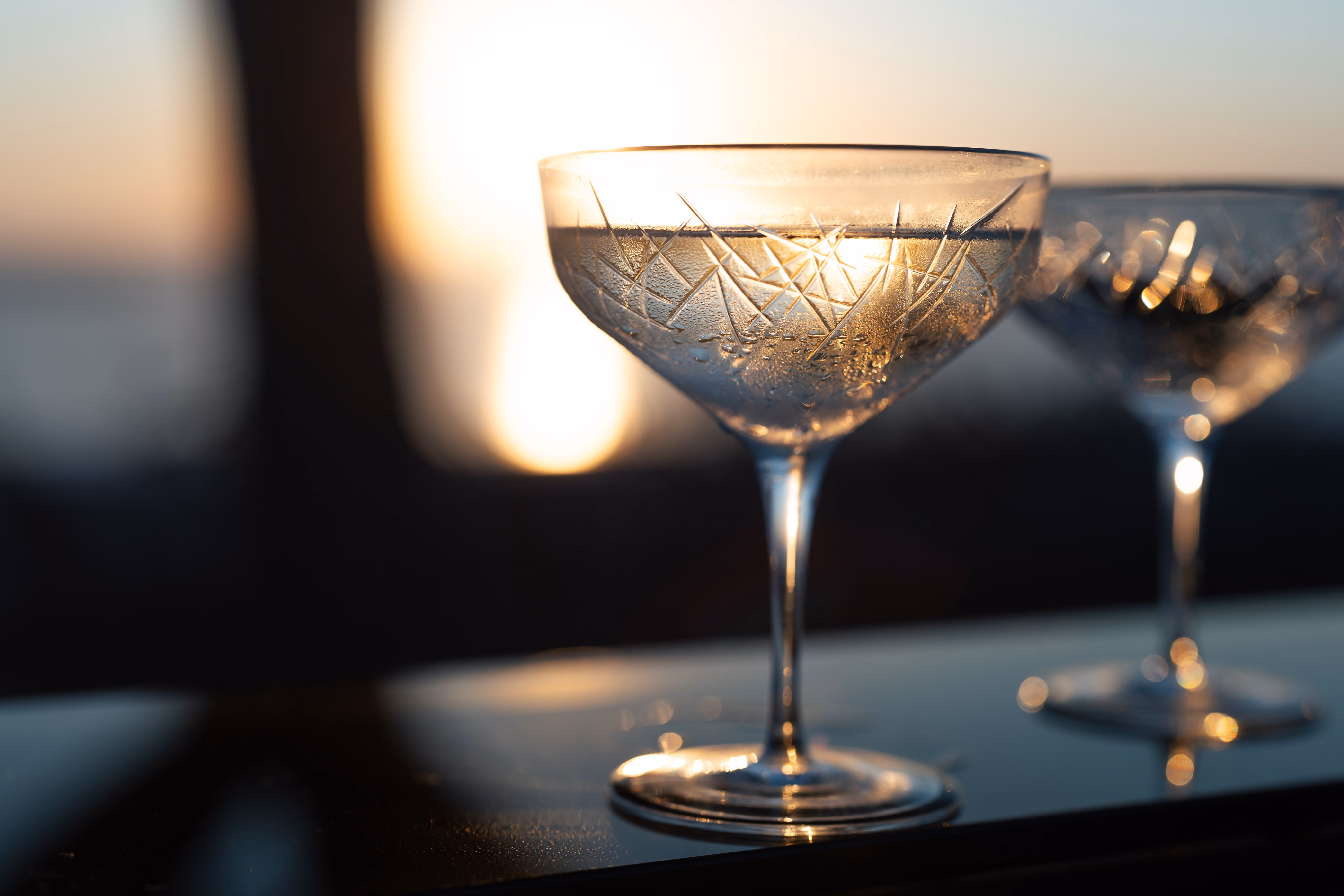 Two etched crystal cocktail glasses with condensation, backlit by a warm sunset.