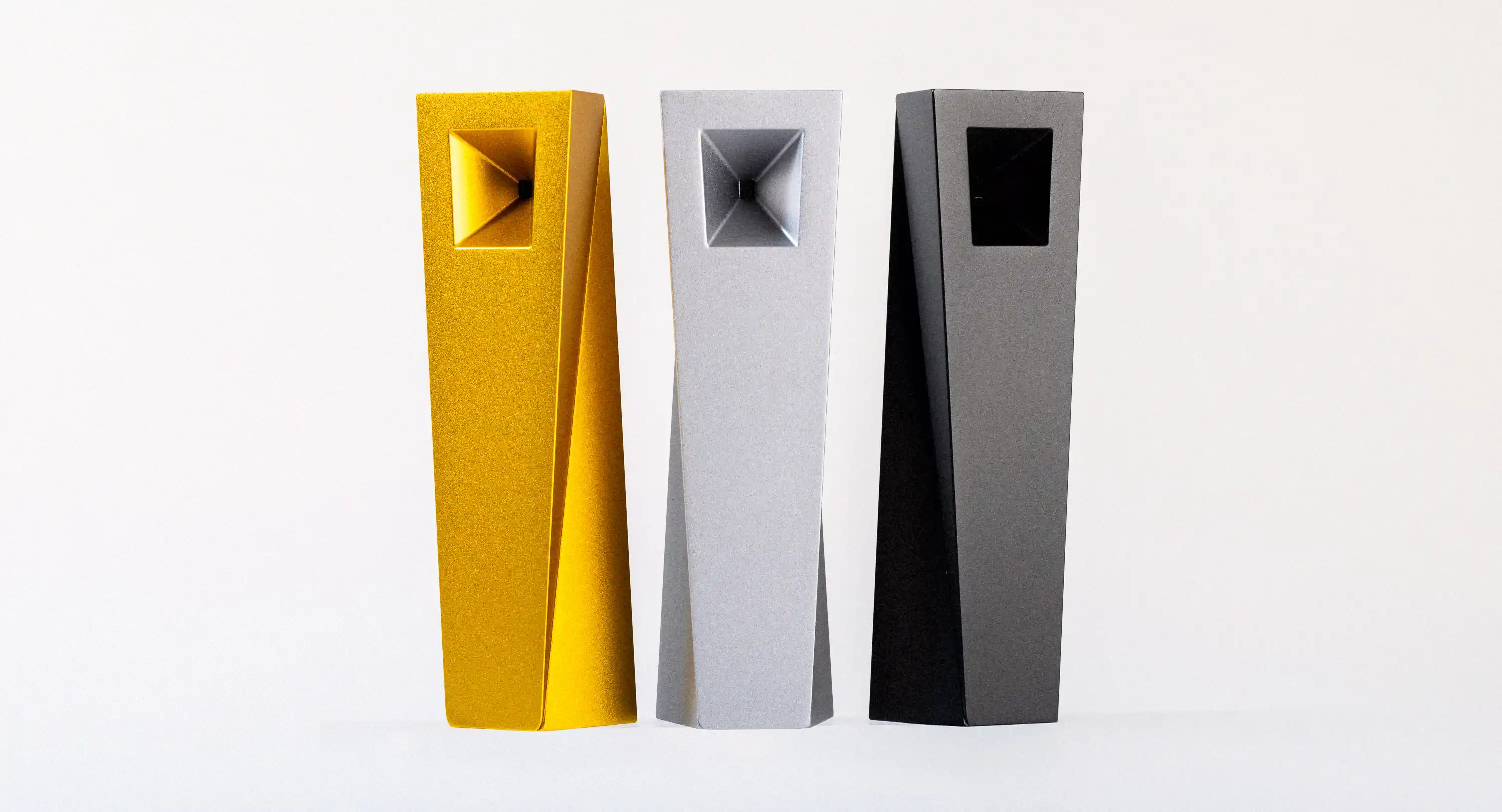 Three Tempest modern smoking pipes in gold, black, and silver finishes standing upright in a white studio