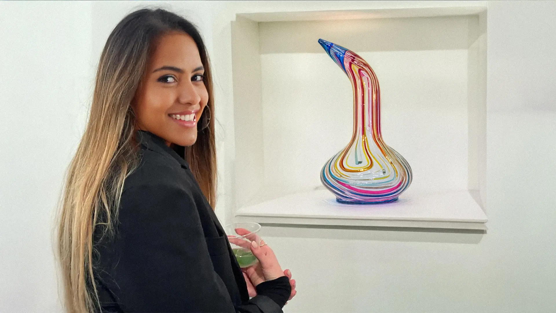 a young woman in an art gallery standing in front of an expensive glass bong on display