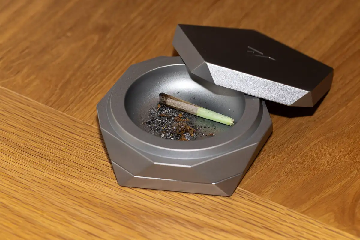 A designer metal ashtray with a lid containing ash and a rolled item