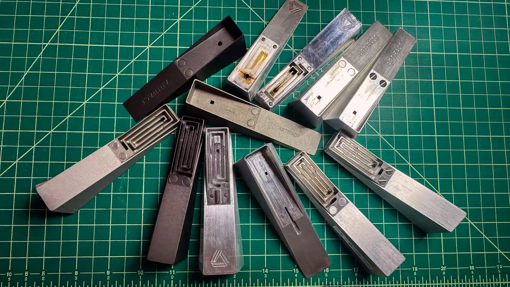Machined aluminum pipe body prototypes on a cutting mat, showing internal pathway variations