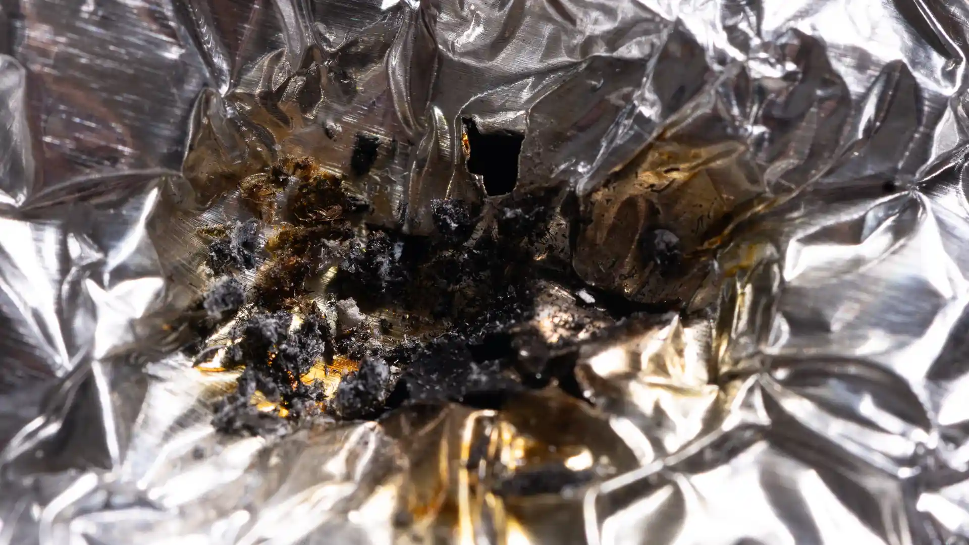 Inside a used aluminum foil bowl, showing ash, burnt residue, and heat discoloration