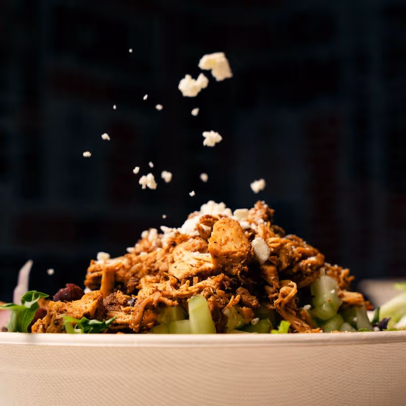 Salad bowl with seasoned shredded chicken and crumbled cheese sprinkled on top.