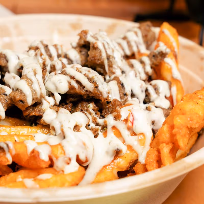 Waffle fries topped with seasoned beef and drizzled with white sauce in a bowl.